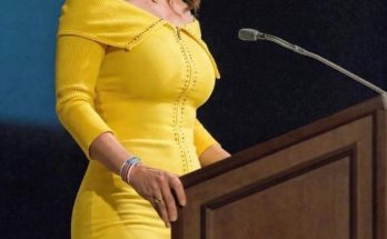sarah Palin wearing a bright yellow off-the-shoulder dress speaks at a wooden podium with