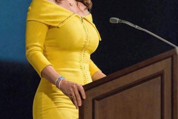 sarah Palin wearing a bright yellow off-the-shoulder dress speaks at a wooden podium with