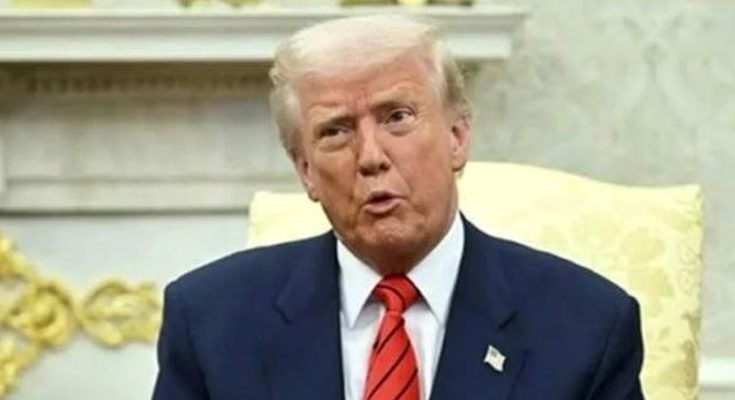 donald Trump seated in formal setting wearing navy suit and red striped tie speaking