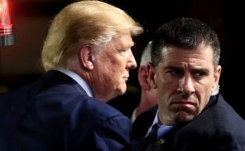 donald Trump and a man in suits facing each other with a red light in the background