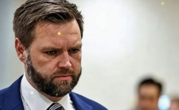 man with beard in blue suit looking down in formal indoor setting