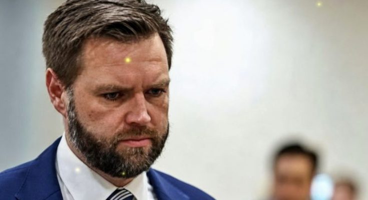 man with beard in blue suit looking down in formal indoor setting