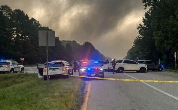 police vehicles with flashing lights block a highway lane behind yellow crime scene tape