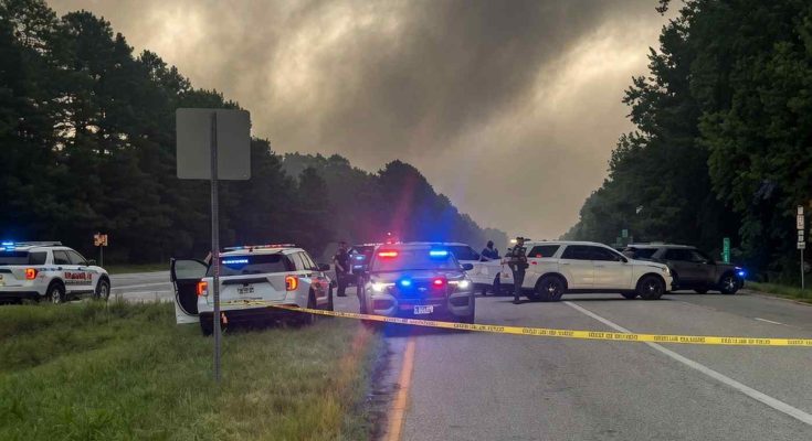 police vehicles with flashing lights block a highway lane behind yellow crime scene tape