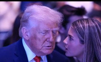 donald Trump in dark suit and red tie listens intently to a young woman with long brown