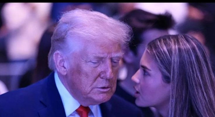 donald Trump in dark suit and red tie listens intently to a young woman with long brown