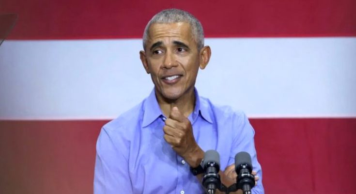 former President Barack Obama speaking at a podium with dual microphones against a red