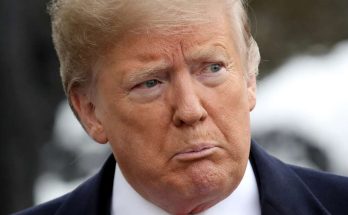 donald Trump in navy suit and red tie with serious expression outdoors