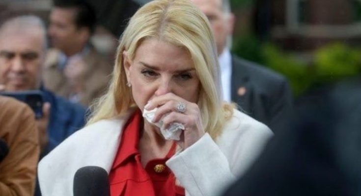 woman with blonde hair in white coat and red blouse wiping tear with tissue at press