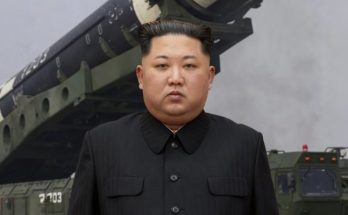 kim Jong Un stands before a large military missile launcher with checkered markings on a
