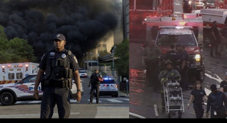 police officer stands before thick black smoke rising from building fire with emergency