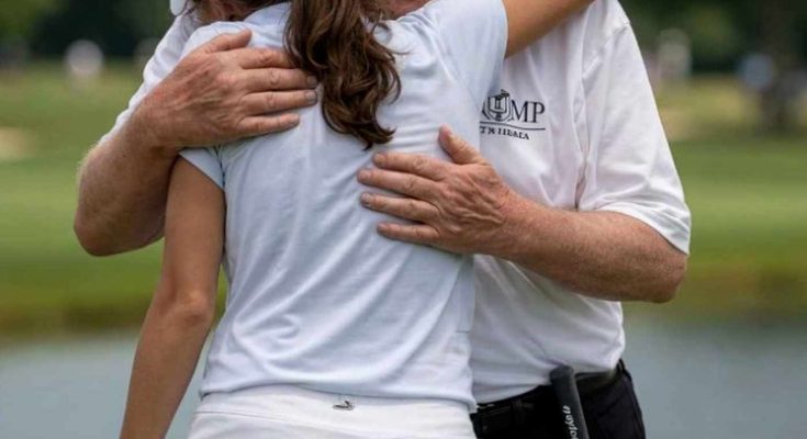 donald Trump wearing red MAGA cap hugging young woman golfer on green with golf clubs