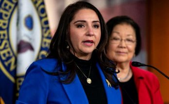 woman in blue blazer speaks at U.S. House of Representatives podium with colleague in red