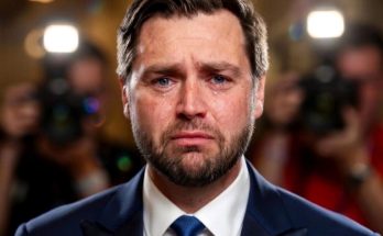 JD Vance with tears on his face during a press event with cameras flashing behind him