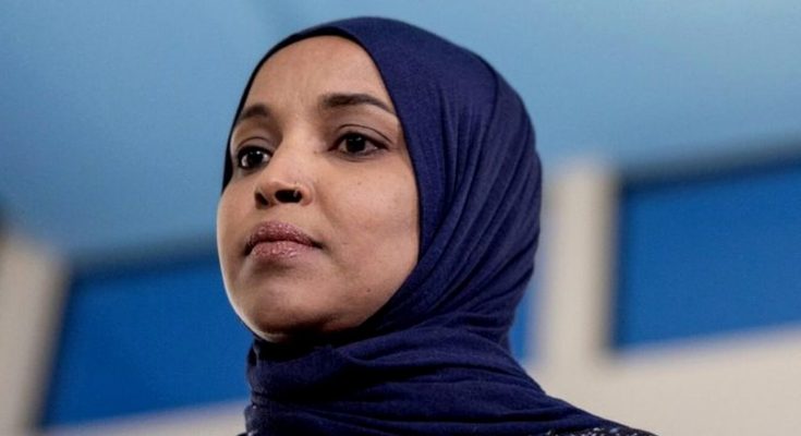 ilhan Omar wearing navy blue hijab at indoor press conference with blue and white