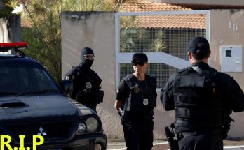brazilian federal police officers in tactical gear stand near a black Mitsubishi patrol