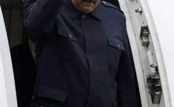 nicolás Maduro raises clenched fist while exiting aircraft doorway in dark blue uniform