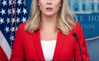 white House press secretary in red blazer at podium with American flag and RESIGNED text