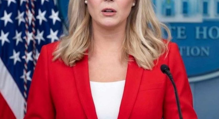 white House press secretary in red blazer at podium with American flag and RESIGNED text