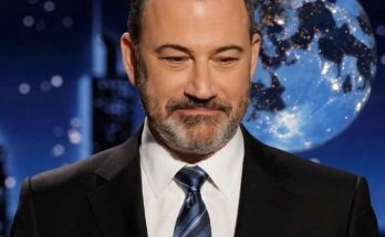 jimmy Kimmel in dark suit and striped tie against blue globe backdrop with city skyline