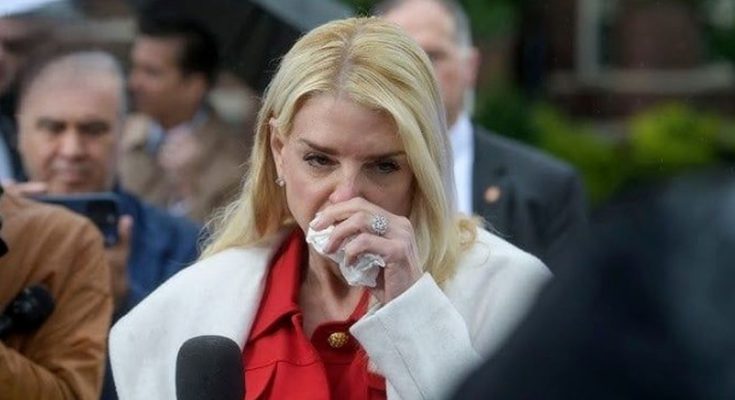 blonde woman in red blouse and white coat wipes eyes with tissue while speaking into